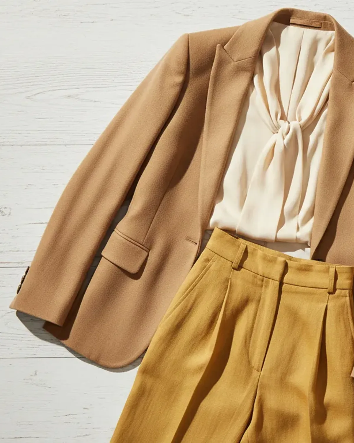 True Spring workwear outfit flat lay: cream blouse, camel blazer, warm navy trousers and gold hoops.